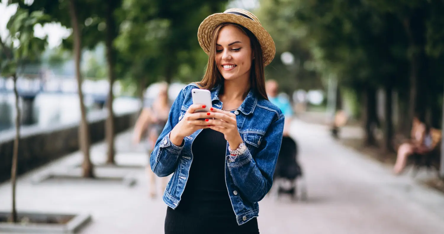 a woman in a hat with veneers smiling while looking at her phone